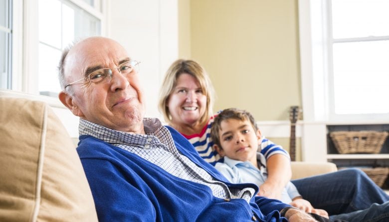 Elderly man in blue sweater with family on sofa