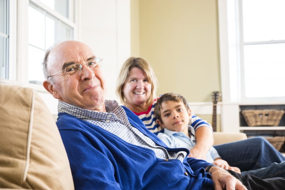 Elderly man in blue sweater with family on sofa