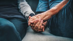 Elderly couple holding hands at home