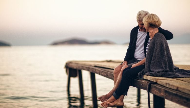 Senior couple sitting together on a jetty.